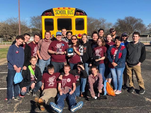 Robotics team posing in front of bus holding their trophies 